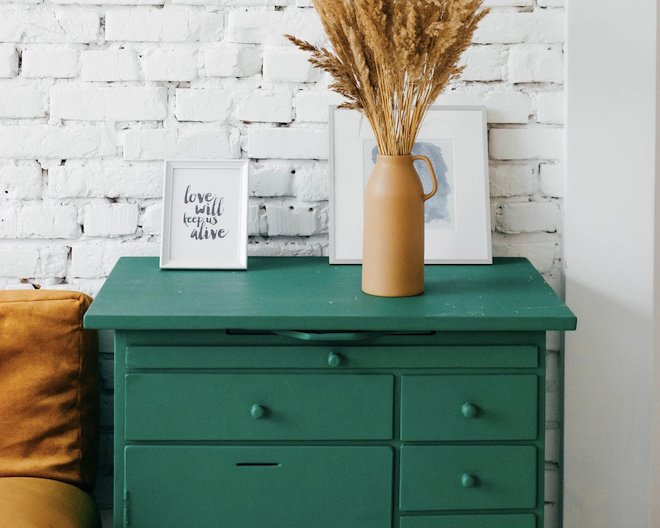 A Picture of a green drawer with some picutre frames and a dried flower on top.